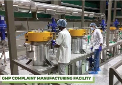Two operators in hairnets and gowns loading an extractor vessel inside a GMP-compliant manufacturing facility.